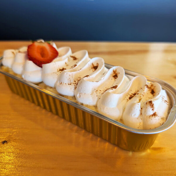 Slice of tres leches cake topped with whipped cream and a slice of strawberry at the top